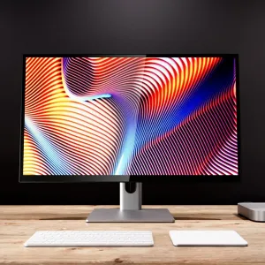 ALOGIC Clarity 27-tommers UHD 4K-skærm på en sølvfarvet stander med farverigt display, på et skrivebord med tastatur og pegefelt.