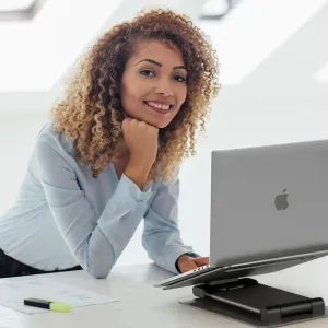 Verstellbarer Alogic Elite Plus Laptopständer mit einem silbernen Laptop auf einem Schreibtisch in einem hellen Büro