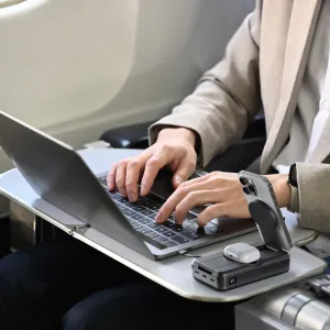 ALOGIC Roam Powerbank mit ausklappbarem Smartphone-Ständer beim Laden eines Smartphones und von Ohrhörern auf einem Flugzeug-Klapptisch