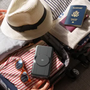 Tragbare ALOGIC Roam Powerbank mit Qi2-Ladepad, abgebildet in einem Koffer mit Reiseutensilien