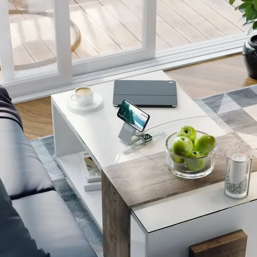 3-i-1 ladestasjon med vinklet magnetisk telefonplate og Apple Watch-puck på lav sokkel, plassert på et salongbord.