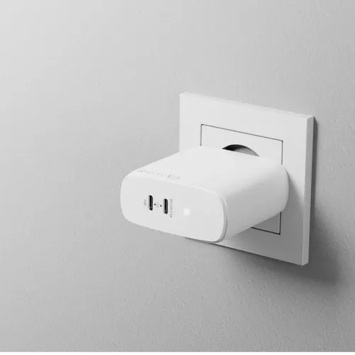 Hvit vegglader med USB-C- og USB-A-porter og LED-indikator, sett i sideprofil og koblet til stikkontakt, kompakt form