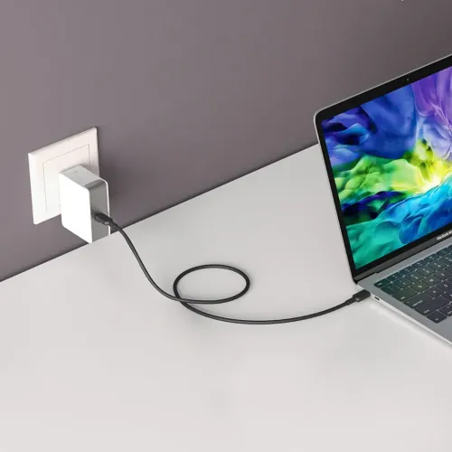 ALOGIC USB-C-väggladdare i vägguttag, vit rektangulär profil; svart USB-C-kabel kopplar till bärbar dator på vitt skrivbord.
