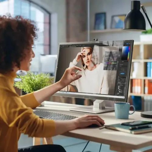 Clarity folding stand under monitor, low profile in silver with cube-shaped joint and rectangular base on desk in studio environment.