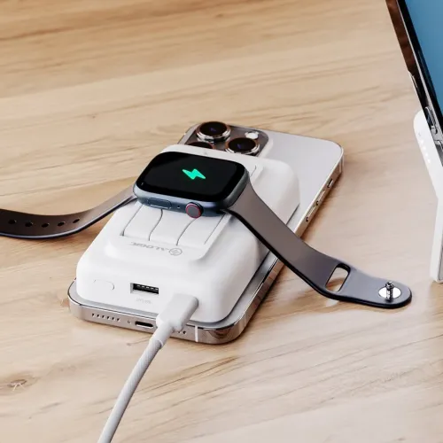 Alogicin valkoinen tehopankki, jossa on käännettävä jalusta ja USB-A-portti, lataa älykellon päälle ja lepää puhelimen päällä pöydällä.