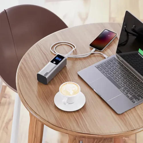 ALOGIC Ark powerbank in silver on round wooden table, with digital display, charges laptop and smartphone via two USB-C cables.