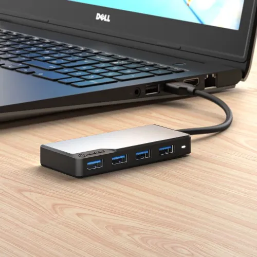 Space gray Alogic USB-A 4-port hub with four blue USB-A ports and small indicator, connected by cable to laptop on wooden table.