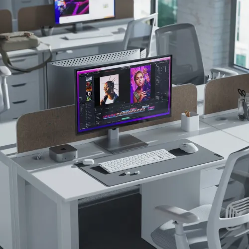 Monitor med tynne rammer på sølvfarget stativ, plassert på skrivebord i kontormiljø ved siden av minidatamaskin, hvitt tastatur og hvit mus.