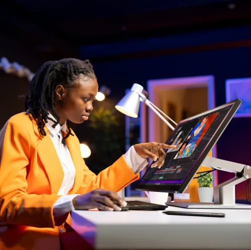 ALOGIC Clarity 27-tommers berøringsskjerm på justerbart armstativ; én person peker på redigeringsvisningen ved skrivebordet med tastatur.