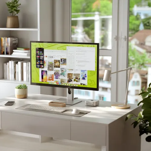 ALOGIC Clarity-skjerm på sølvfarget stativ med tynne rammer, på skrivebordet ved siden av tastatur, styreflate og lampe foran vinduet