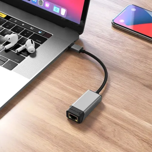 USB-C till RJ45-adapter med kort flätad kabel och metallhus, ansluten till laptopens USB-C-port; porten syns på skrivbordet.