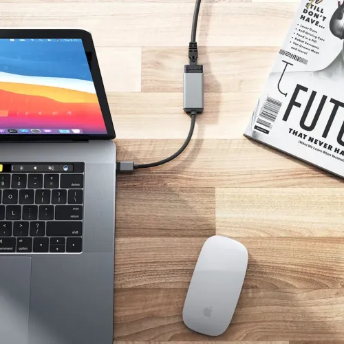 USB‑C till RJ45 Ethernet-adapter ansluten till bärbar dator, med nätverkskabel inkopplad, på träbord med mus och magasin.