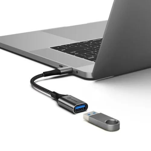 USB-C till USB-A-adapter i rymdgrå metall med flätad kabel, ansluten till laptop; USB-minne placerat framför på vit yta.
