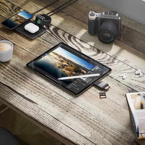 USB-C till SD/MicroSD-kortläsare i grått ansluten till surfplatta; SD-kort isatt, microSD bredvid, låg profil på träbord.