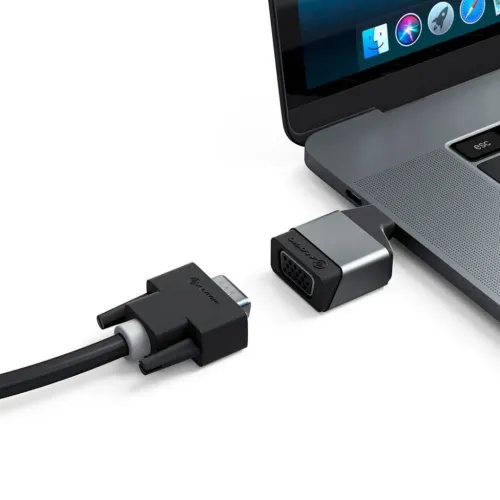 USB-C till VGA-adapter i metall, ansluten till bärbar datorns USB-C-port, med VGA-hona riktad mot en lös VGA-kabelkontakt.