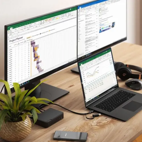 Svart dockningsstation på skrivbord, ansluten till bärbar dator och två monitorer; rektangulär med statuslampor och portar.