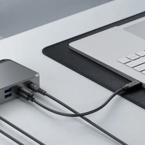 ALOGIC PRIME DX2 Universal Dock, kabeliais prijungtas prie nešiojamojo kompiuterio ant stalo, kompaktiškas pilkas darbo vietos šakotuvas.