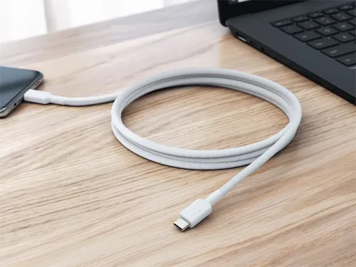 Cable ALOGIC Elements PRO de USB-C a USB-C, cordón trenzado blanco enrollado sobre un escritorio y conectado a un portátil y a un teléfono