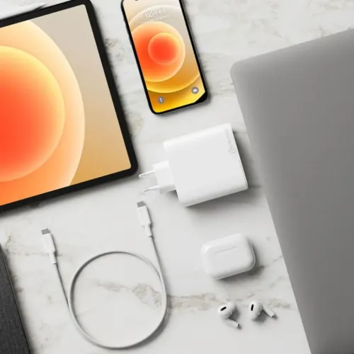 Vit ALOGIC-väggladdare med två runda stift ligger på marmoryta bredvid USB‑C‑kabel, surfplatta, mobil, laptop och hörlurar.