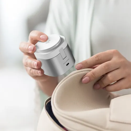ALOGIC Powerpod, cylindrisk vit/silver laddningsstation med USB‑C-port och nedfällt stativ, hålls över en öppen beige väska.