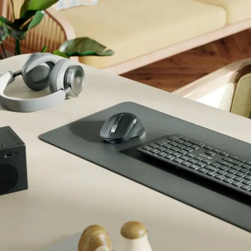 Must ergonoomiline hiir kahe kerimisrattaga ja külgmiste nuppudega, mis on asetatud tumedale vaibale klaviatuuri kõrvale heledale lauapinnale.