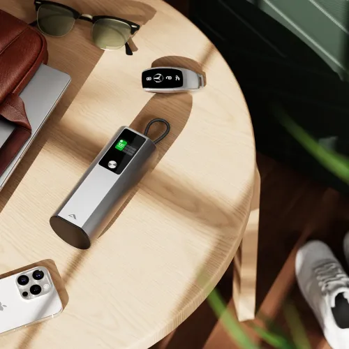 Silverfärgad powerbank med inbyggd loopkabel och display som visar 100%, liggande på en träbordsskiva bredvid smartphone.