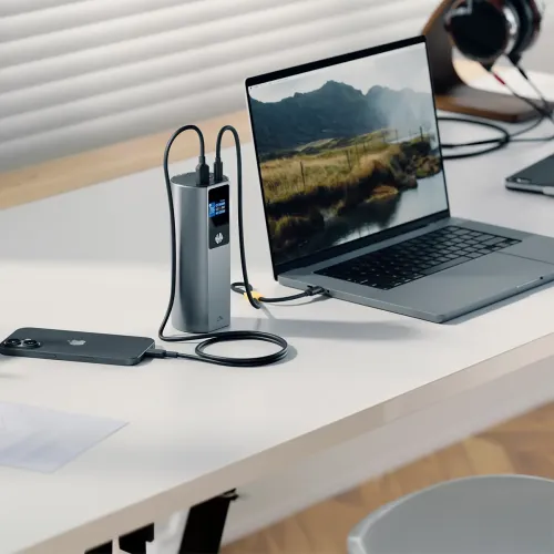 ALOGIC Ark Pro power bank charging a laptop and smartphone on a desk, with a built-in display and cables attached.