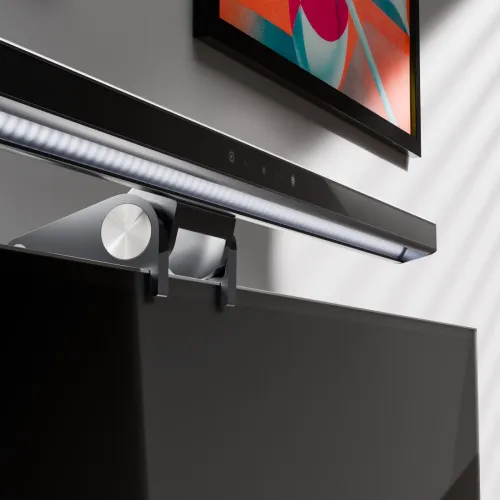 Ljusramp med inbyggd kamera på skärmens överkant, med LED-rad undertill, touchikoner framtill och klämfäste i metall, grå.