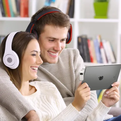 Hvid lydsender forbundet med et kort kabel til hovedtelefonstikket på tabletten, rektangulær med en lille skærm og knap i kanten af billedet.