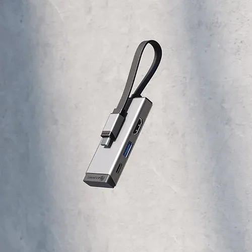 Sidabriškai pilkas "3-in-1" USB-C adapteris su HDMI, USB-A ir USB-C prievadais, šone pritvirtintu dirželiu su USB-C jungtimi, pilkame fone.